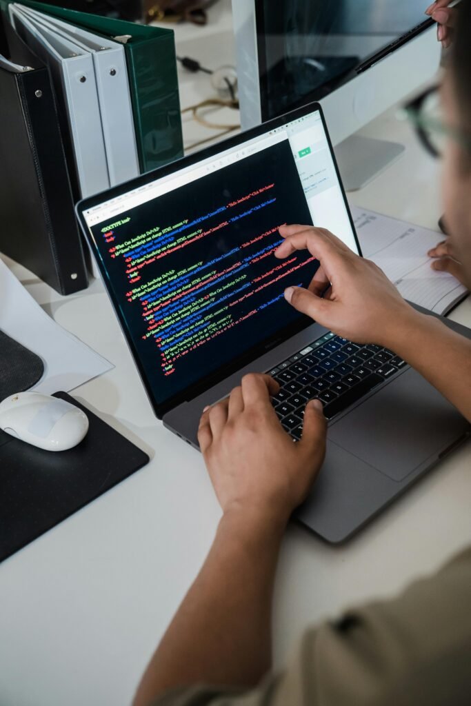 pexels-photo-12899188-12899188 Close-up of a programmer pointing at a colorful code script on a laptop in an office setting.