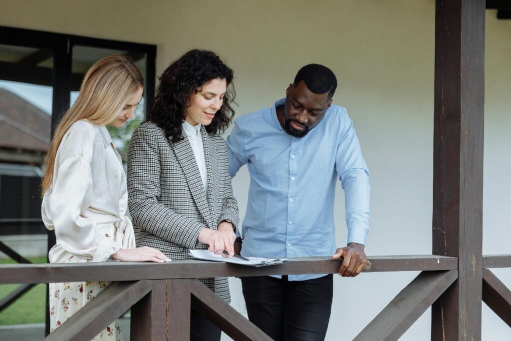 Real estate agent discussing property paperwork with a couple on a porch.